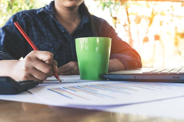 A person sitting at a desk reviewing financial documents with a calculator, computer, and coffee cup present, illustrating careful budget planning and financial analysis.