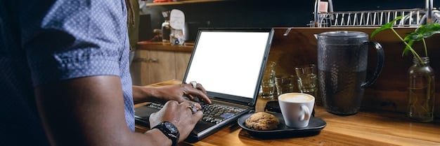 A person working on a laptop at a coffee shop. The screen shows a budget spreadsheet with income and expense categories. A cup of coffee and a notebook are on the table, conveying a sense of productivity and financial planning.